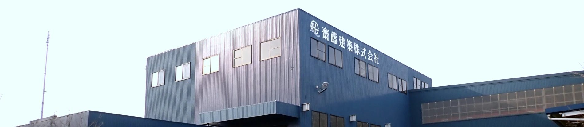 「齋藤建築株式会社」の看板がある、紺色の工場の外観