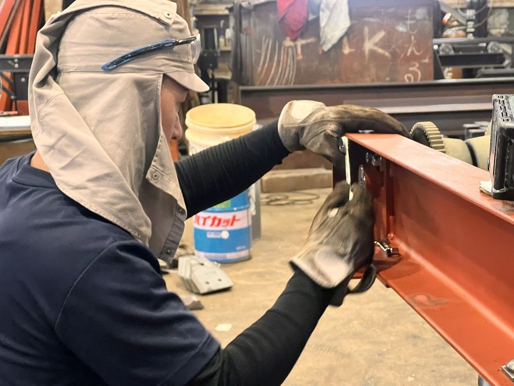赤い鉄骨の部材を工具で仕上げる社員