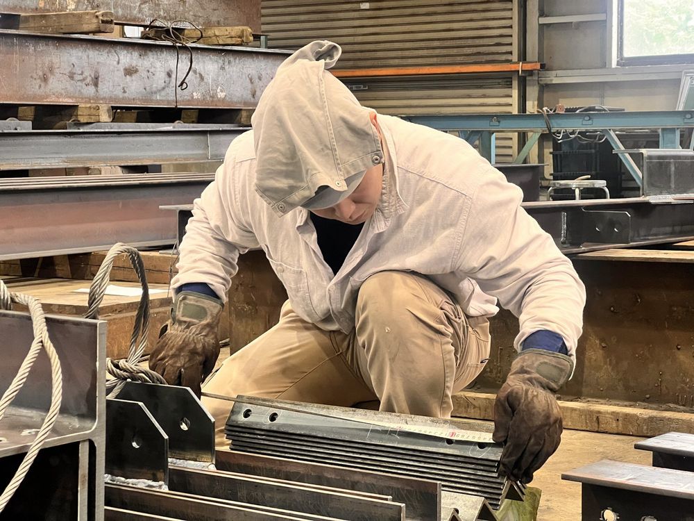 鉄骨の部材を前に、しゃがんで作業する社員